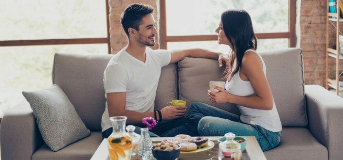 couple in casual outfit is sitting on sofa indoors and smiling