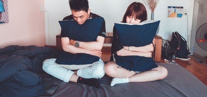 Couple Hugging Pillows While Sitting on the Bed