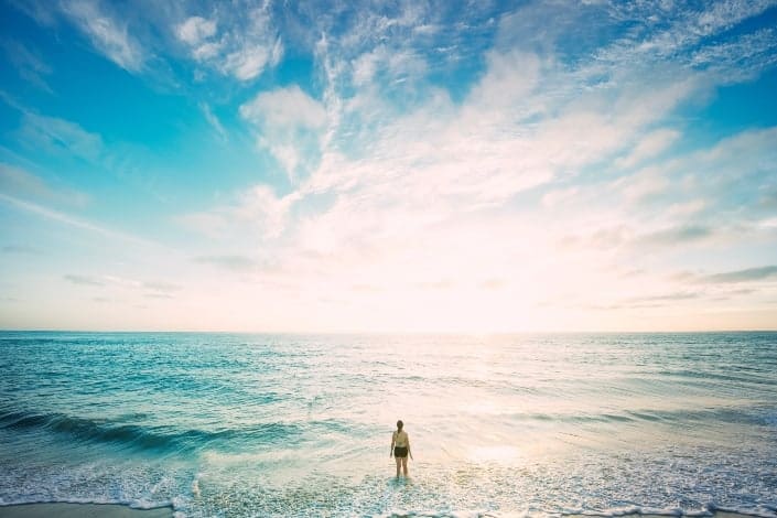 Girl standing at beach staring into sunny sky