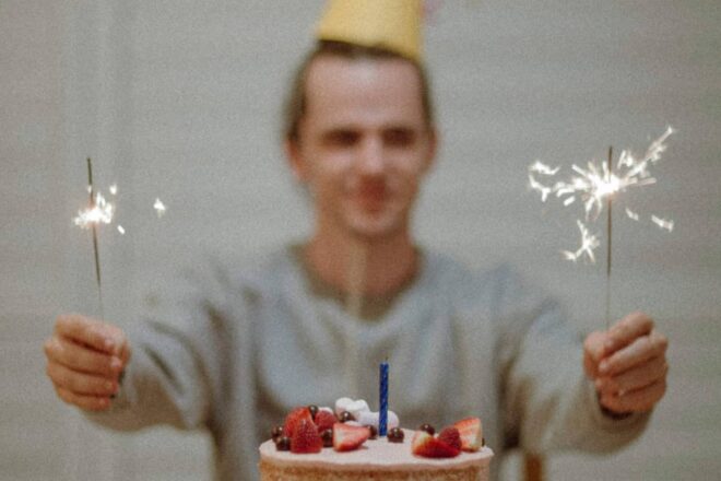 man wearing party hat holding sparklers with birthday cake - birthday gifts for boyfriend