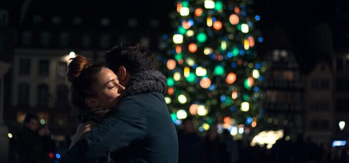 man and woman hugging at night with christmas tree in the background