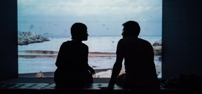 Couple sitting in front of beach scene on white screen.