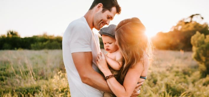 husband and wife with baby in the middle outdoors