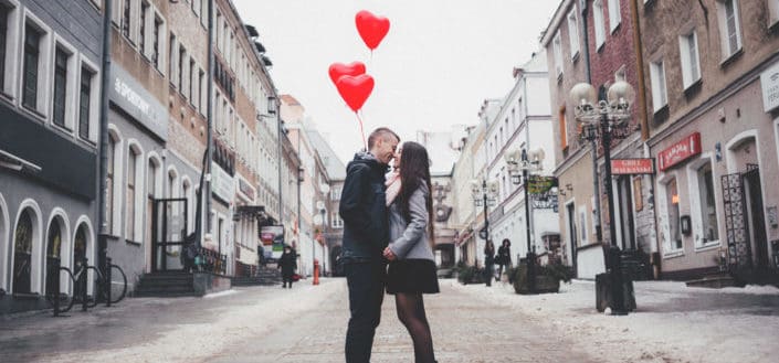 Sweet couple in the middle of the street holding red heart-shaped balloons