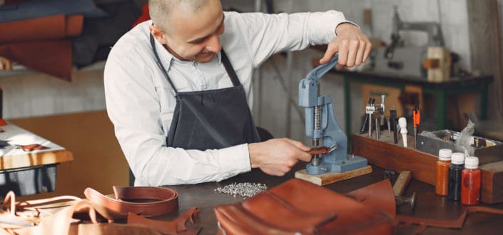 A bald tailor man punching a hole on a belt 