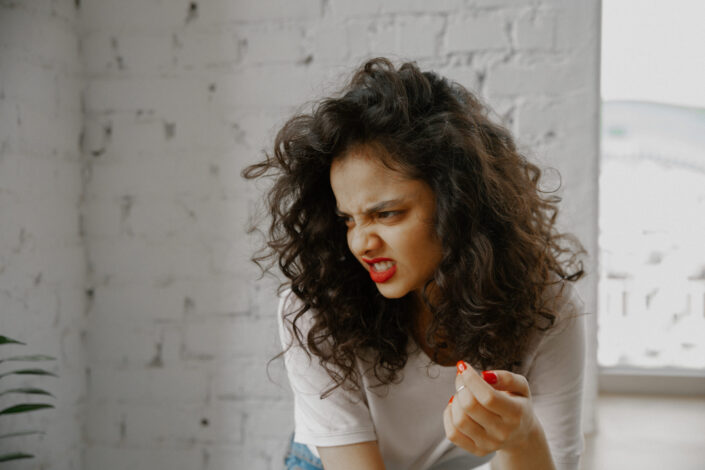 Girl with a red lipstick and nails, scowling.