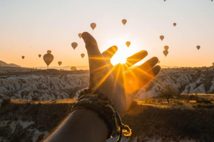 Person's Hand Across Flying Hot Air Balloons
