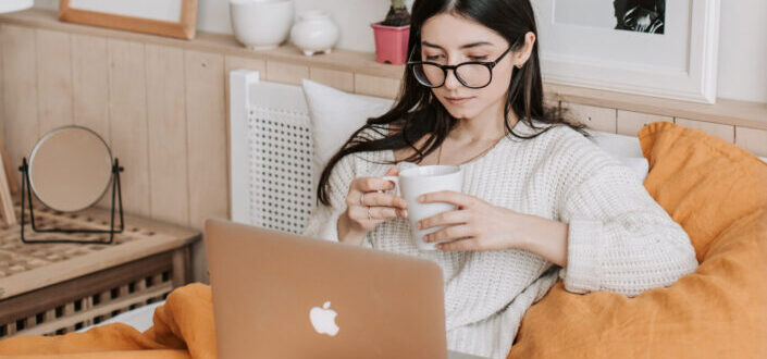 girl using laptop with mug in her bedroom.