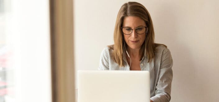 Mature woman typing on a laptop wearing earphones.