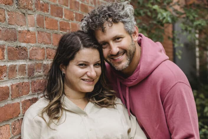 Mature couple smiling next to a brick wall.