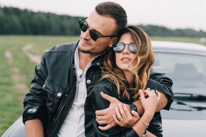 couple clinging while sitting on hood of car.