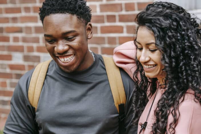 Joyful multiethnic teens laughing while sharing smartphone
