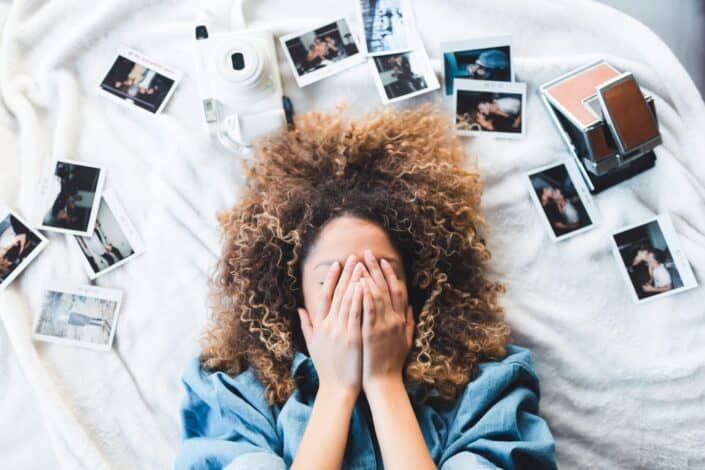 woman laying in a bed full of polaroids while covering her face
