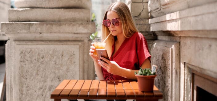 woman drinking while holding smartphone