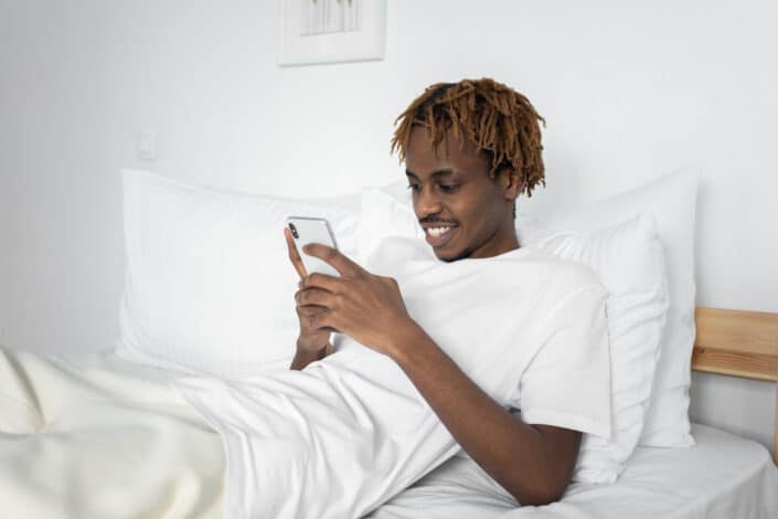 man in white using smartphone on his bed