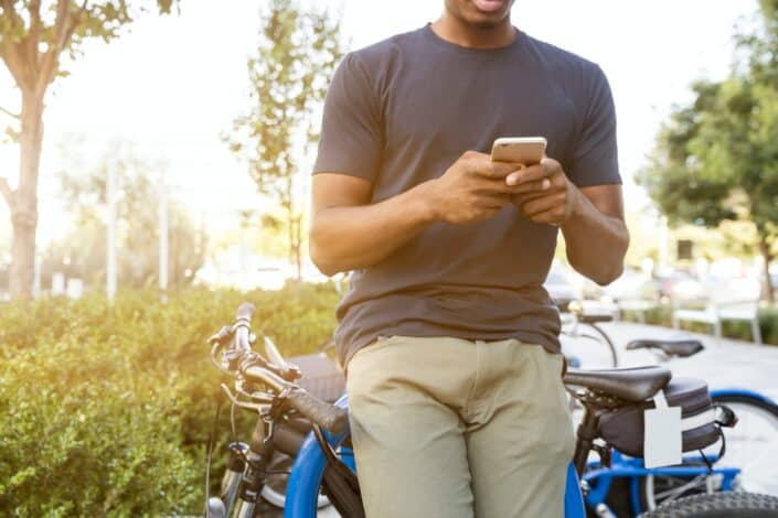 man holding smartphone leaning on bicycle 