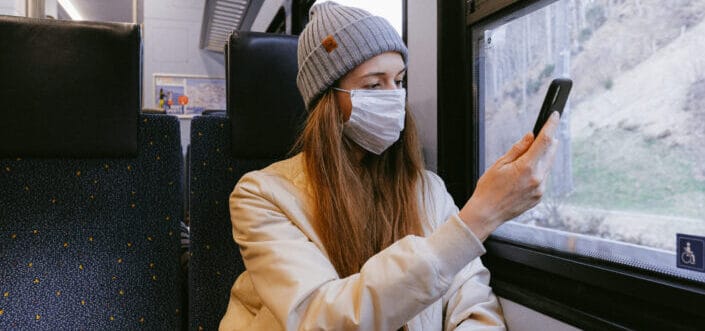 Woman wearing a face mask sitting beside the window inside a train checking at her phone