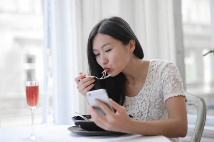 Woman staring at her phone while eating noodles