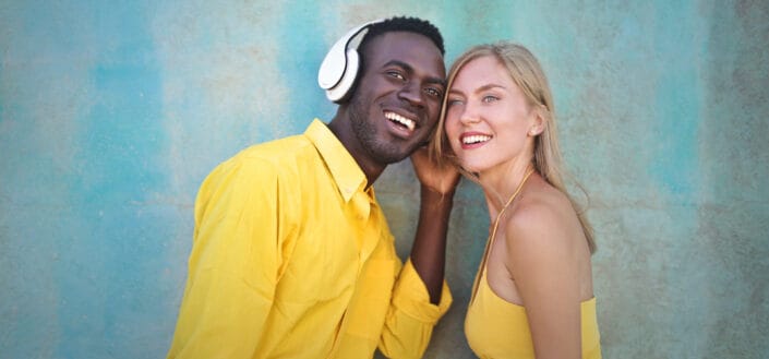 Couple both wearing yellow listening to music over one headphone