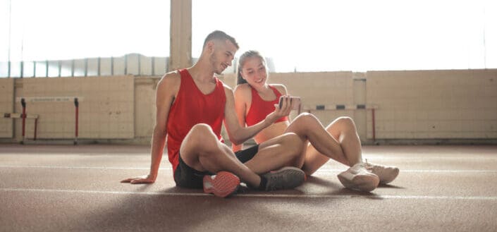 Couple wearing running outfit sits on the floor while looking at something in the phone