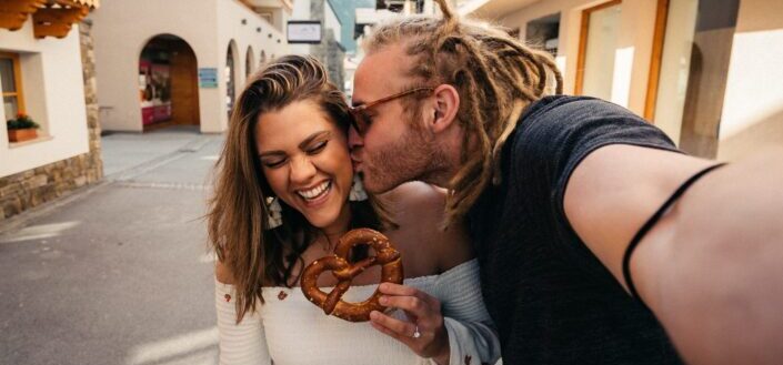 Man kissing a woman whose holding a pretzel