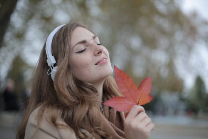 A woman with headphones feeling the music while holding a leaf.