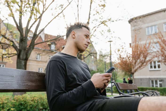 Man sitting on a park bench while holding his phone