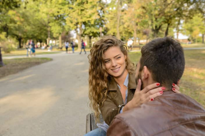 Woman gently holding the face of her man on a park bench.