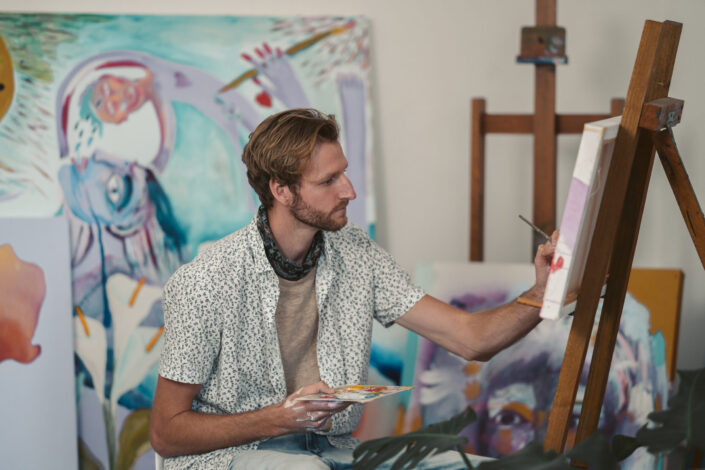 An artist painting on a canvas while holding a color palette