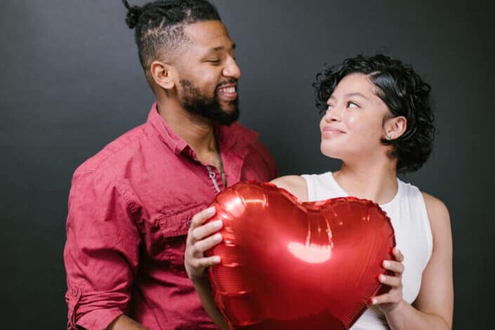 Couple looking at each other while holding a red heart shaped balloon