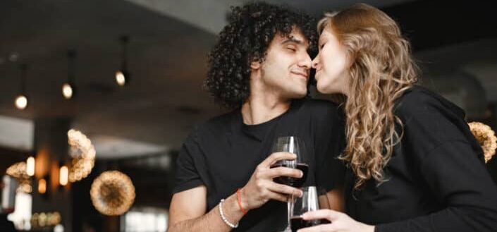 Man and woman holding a glass of wine about to kiss