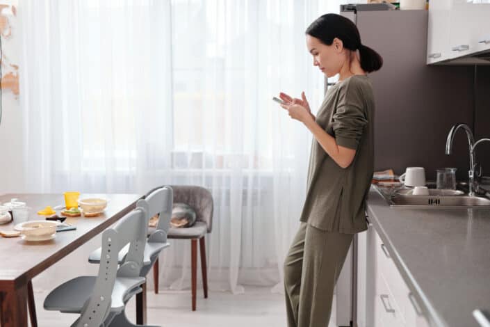 Woman in kitchen browsing on her celfone