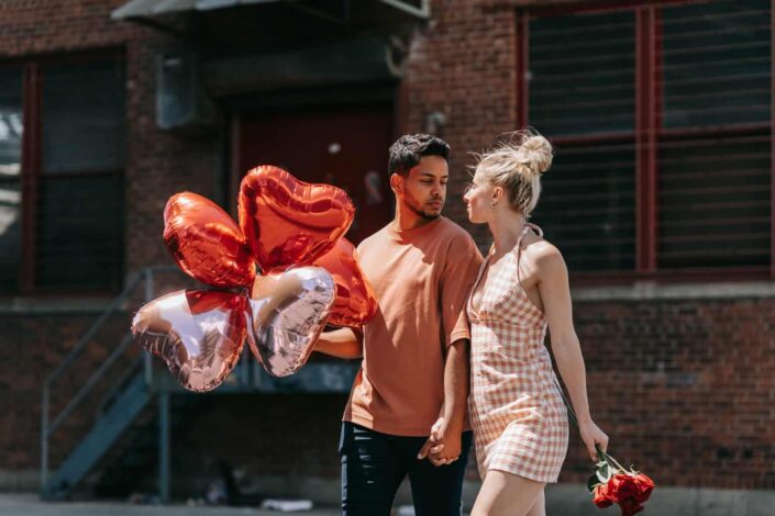 man staring at his girlfriend while holding heart-shaped balloons