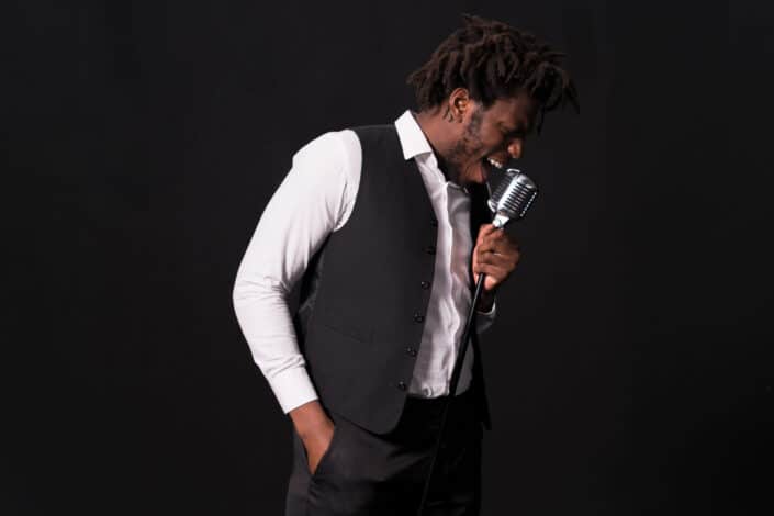 Dark skinned man singing on a mic