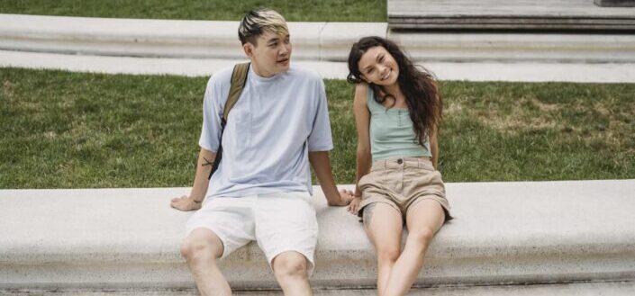 Cheerful multiethnic couple resting on urban bench in summer