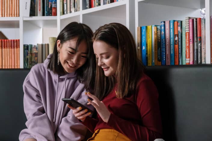 Girl in Red Sweater Holding Her Phone While Talking to Her Friend