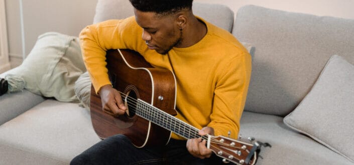 A man in a yellow sweater playing the acoustic guitar