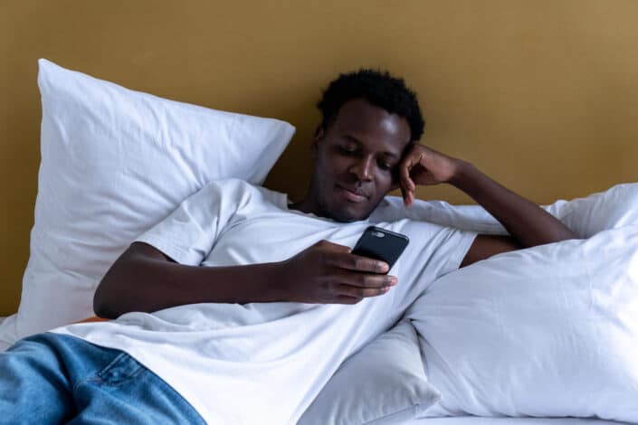 A man lying on the bed while using his mobile phone