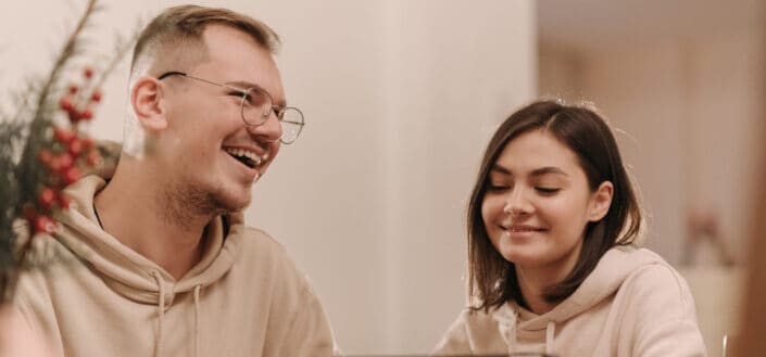 Man and woman in beige hoodie laughing in front of an ipad