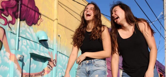 Two laughing women walking past graffiti wall