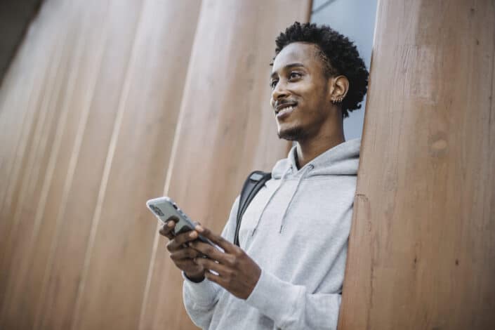 Smiling black man with phone standing near wall