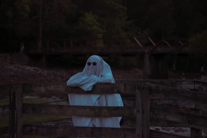 a ghost leaning on a wooden fence