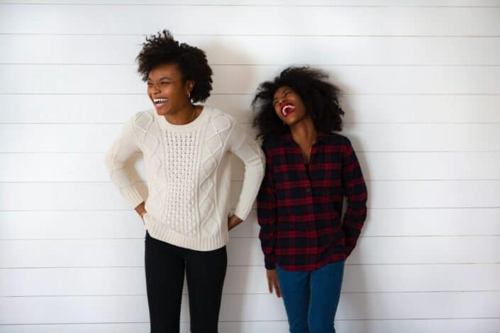 Two ladies laughing while standing against the wall
