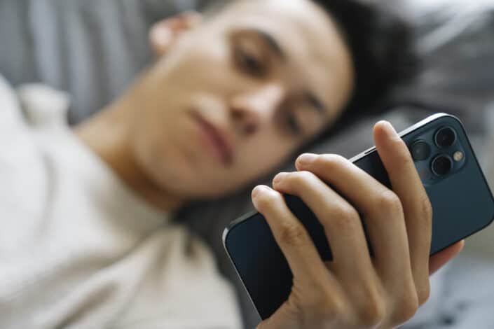 Young guy browsing mobile phone on bed