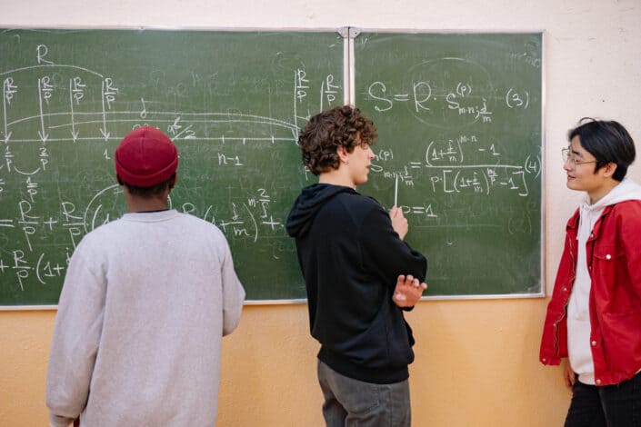 Young men standing beside blackboard