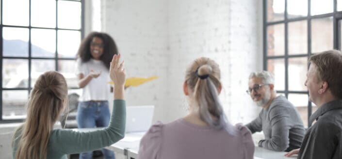 Female employee raising hand for asking question at conference in office boardroom