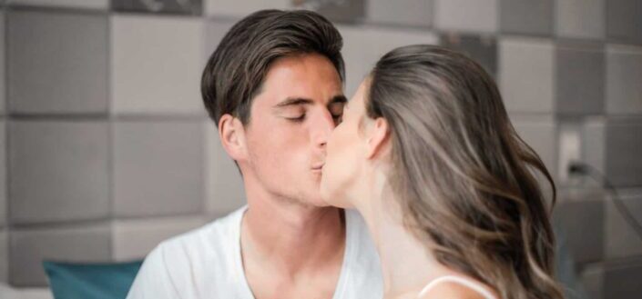 Photo of man in white crew neck t shirt kissing woman in white tank top
