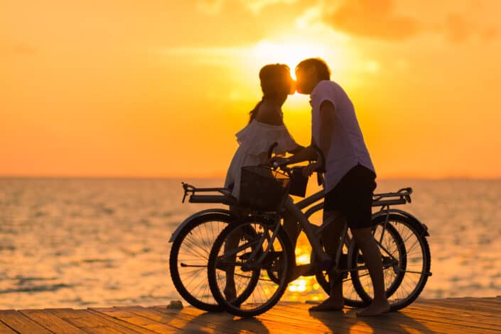 Man kissing a woman on a bicycle during sunset