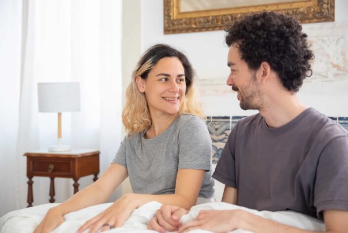 Man and woman sitting on bed smiling
