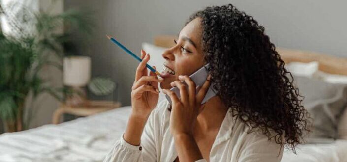 Woman Using a Smartphone With a Pencil in Her Mouth